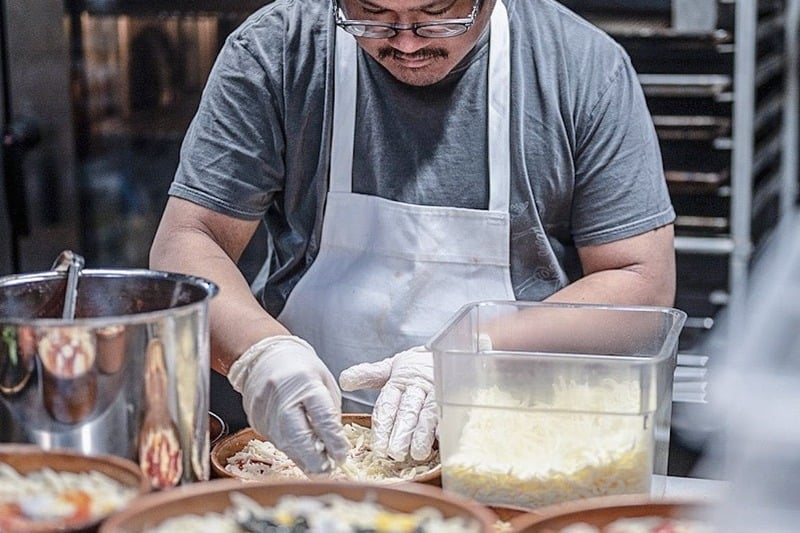 Person making a pizza and wearing a white apron